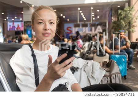 Female traveler reading on her cell phone while waiting to board a plane at departure gates at 50854731