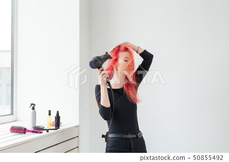 Stylist, fashion, hairdresser, people concept - woman drying her colored hair near the window 50855492