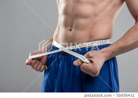 Athletic young man with perfect abs measuring his waist 50856432