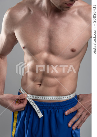 Strong athletic young man with perfect body measuring his waist 50856433