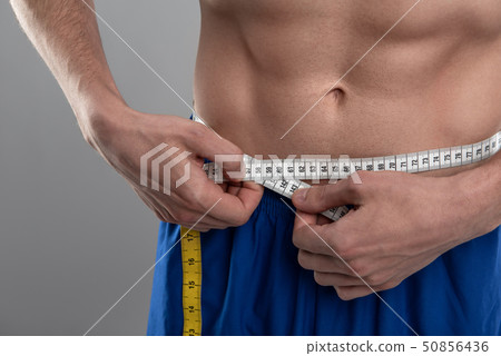 Young man with perfect abs measuring his waist 50856436
