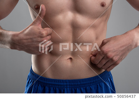 Young man demonstrating his six-pack abs and showing thumbs up 50856437