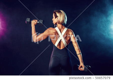 Back view of a sporty woman in fashionable sportswear does the exercises with dumbbells. Photo of Back view of a sporty woman in fashionable sportswear does the exercises with dumbbells. Photo of 50857079