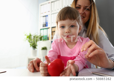 Little baby girl visiting doctor holding in hands red toy heart Little baby girl visiting doctor holding in hands red toy heart 50865162