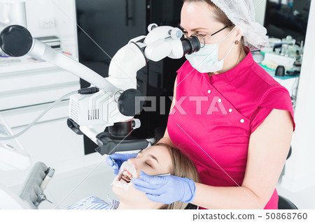 A female professional dentist examines a female patient with a stamotologic microscope in her office 50868760