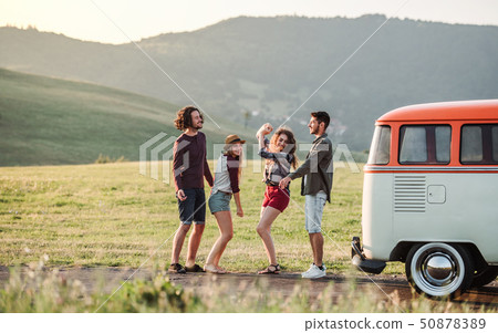 A group of friends standing outdoors on a roadtrip through countryside, dancing. 50878389