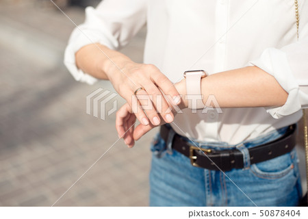 Woman wearing white shirt wearing blue jeans and a gentle nude manicure looks at the watch close-up. 50878404