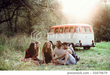 A group of friends sitting on ground on a roadtrip through countryside, having picnic. 50878679