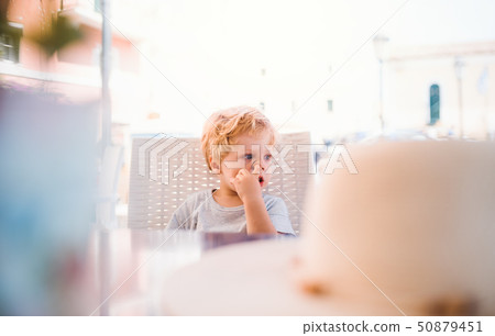 Small boy sitting in outdoor restaurant on summer holiday, picking nose. Small boy sitting in outdoor restaurant on summer holiday, picking nose. 50879451
