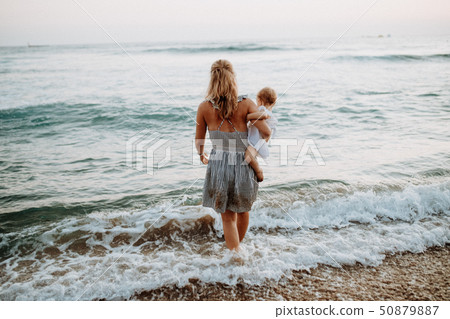 Rear view of young mother with a toddler girl walking in sea on summer holiday. Rear view of young mother with a toddler girl walking in sea on summer holiday. 50879887