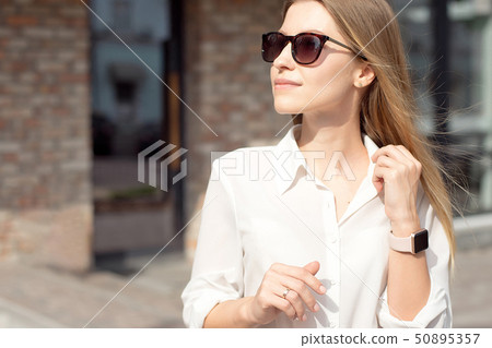 Portrait of a successful happy business woman in a white shirt and sunglasses. Smart watch on a hand Portrait of a successful happy business woman in a white shirt and sunglasses. Smart watch on a hand 50895357