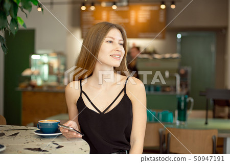 Young beautiful blonde with long hair in a charm top and jeans drinks coffee and looks out the 50947191