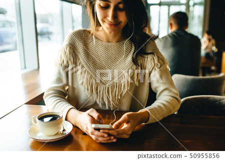 Girl drinking coffee and listening to music in the cafe 50955856