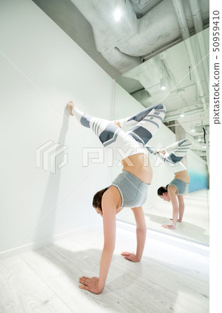 Woman wearing white and grey leggings practicing arm stand 50959410