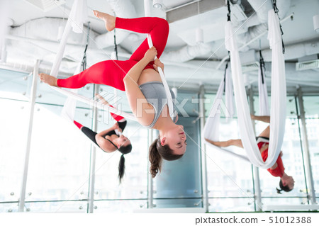 Dark-haired trainer in red leggings showing nice aerial yoga pose Dark-haired trainer in red leggings showing nice aerial yoga pose 51012388