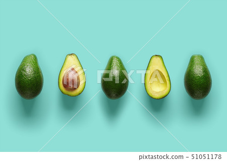 Row of fresh wholes and halves of organic avocado with kernels in center on blue backgrond. Top view 51051178