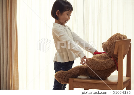 Girl playing with a big bear sitting on a chair 51054385