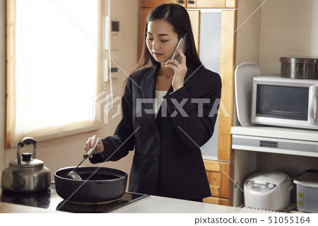 Mother preparing dinner while having phone in the kitchen 51055164