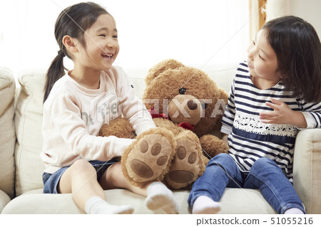 Sisters playing with a big bear on the couch 51055216