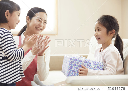 Girl receiving a present from mother and sister on your birthday 51055276
