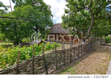 A wicker fence with a garden and a house under a t A wicker fence with a garden and a house under a t 51073697
