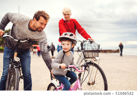 Young family and small daughter with bicycles outdoors on beach. 51086582