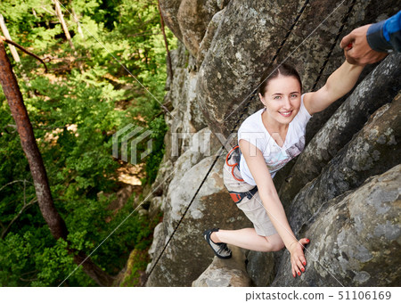 Happy woman climbing rock trekking outdoors. Carefree hiker smiling her friend. Man helping to climb Happy woman climbing rock trekking outdoors. Carefree hiker smiling her friend. Man helping to climb 51106169