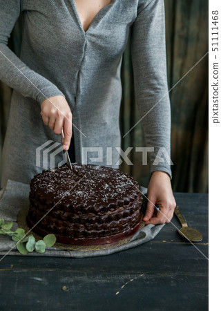 Woman cuts chocolate cake close. Dark tones 51111468