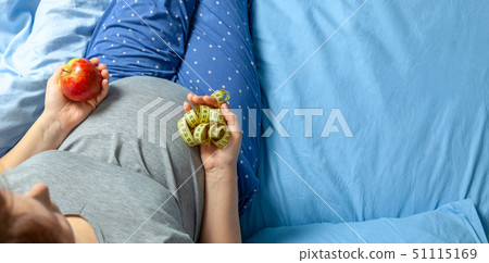 Pregnant woman with a stomach and holding an apple and yellow measuring tape. Diet for pregnant Pregnant woman with a stomach and holding an apple and yellow measuring tape. Diet for pregnant 51115169