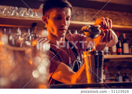Dark-haired bartender squeezing lemon juice into shaker 51123028