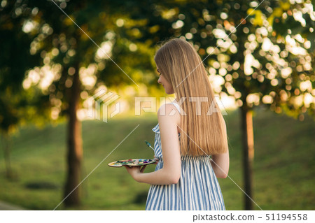 Beautiful girl artist is standing in the park and holding palette with paints 51194558