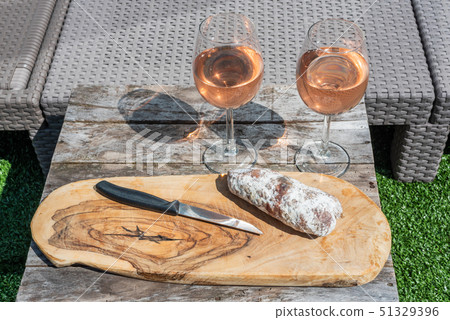 Two glasses of rose wine and a dried sausage with a knife on a wooden table Two glasses of rose wine and a dried sausage with a knife on a wooden table 51329396