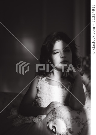 Sun rays fall on the face of little girl. Beautiful little model in studio with natural light Sun rays fall on the face of little girl. Beautiful little model in studio with natural light 51334913