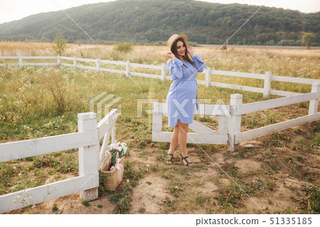 Pregnant woman in nature try on knitted hat. Background of field and white fance near the farm 51335185