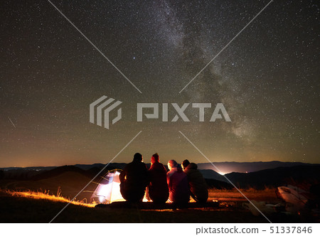Friends resting beside camp, campfire under night starry sky 51337846