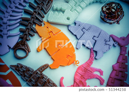 Many bright multi-colored objects printed on 3d printer lie on flat surface 51344238