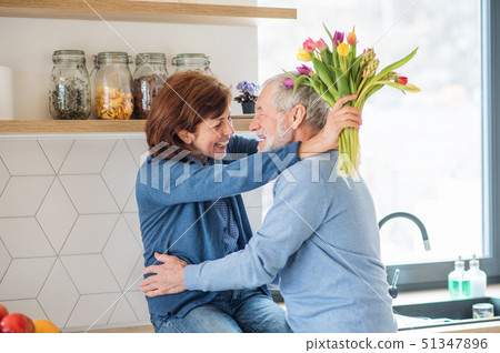 A senior couple in love indoors at home, man giving flowers to woman. A senior couple in love indoors at home, man giving flowers to woman. 51347896