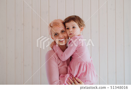 A young woman with small daughter, white wooden wall in the background. 51348016