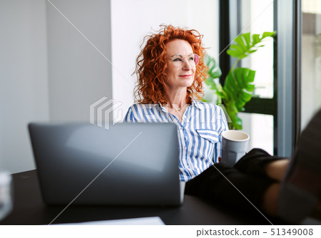 A portrait of businesswoman resting in an office, holding a cup of coffee. 51349008