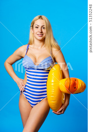 Photo of blonde woman in striped bathing suit with lifebuoy duckling in her hand on empty blue 51352248