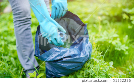 Picture of woman in rubber gloves picking up dirty plastic bottle in bag on green lawn Picture of woman in rubber gloves picking up dirty plastic bottle in bag on green lawn 51352256
