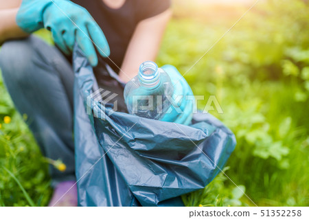 Photo of woman in rubber gloves picking up dirty plastic bottle in bag on green lawn Photo of woman in rubber gloves picking up dirty plastic bottle in bag on green lawn 51352258