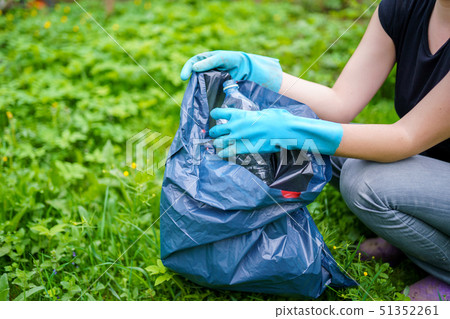 Photo of woman in rubber gloves picking up dirty plastic bottle in bag on lawn Photo of woman in rubber gloves picking up dirty plastic bottle in bag on lawn 51352261
