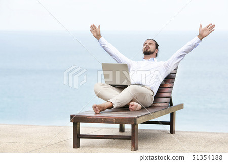 Young businessman on the beach resting on his deck chair using his tablet 51354188