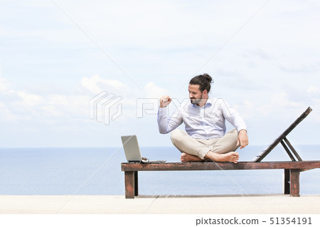 Young businessman on the beach resting on his deck chair using his tablet 51354191