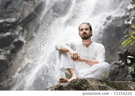 Wellness yoga meditation concept. Young man sitting in lotus position on the rock under tropical Wellness yoga meditation concept. Young man sitting in lotus position on the rock under tropical 51354220