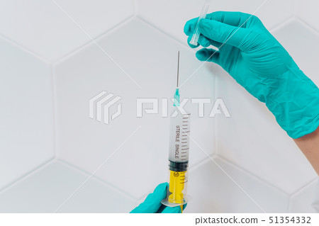 Hands in rubber gloves hold a disposable medical syringe with the drug 51354332