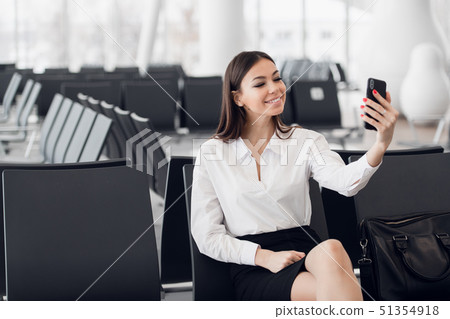 Young business woman at international airport, making selfie with mobile phone and waiting for her 51354918