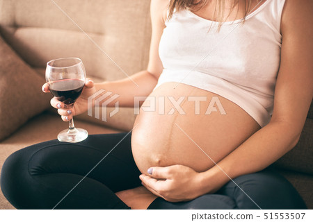 Young future mother sitting at home and drinking alcohol Young future mother sitting at home and drinking alcohol 51553507