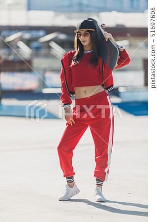 Portrait of young female wearing black hat, red clothing skateboarder holding her skateboard. Woman Portrait of young female wearing black hat, red clothing skateboarder holding her skateboard. Woman 51697608